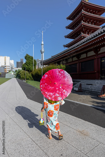 Woman in a kimono carries a red parasol walking at Senso-ji Temple in Asakusa, Tokyo, Japan, with the Tokyo Skytree in the background view.