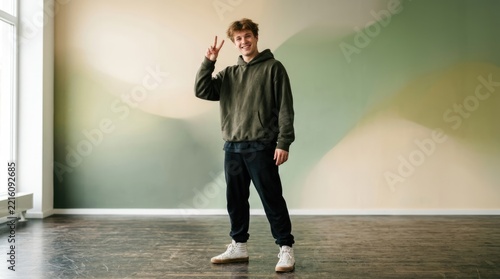 Young Man Giving Peace Sign in Modern Studio with Abstract Wall