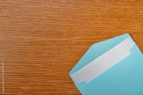 Open blue envelope with a blank white paper card inside on a wooden table. Mail, invitation, letter, newsletter, or business contact concept. Copy space for text.