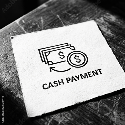 Cash payment icon and text printed on square white paper over dark rustic wooden table for finance and retail business concept.