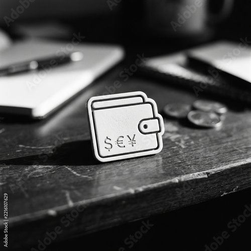 Minimalist black and white concept of a wallet icon with global currency symbols on a wooden desk.