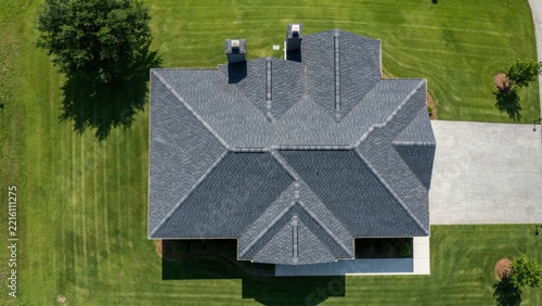 Aerial view of asphalt shingle roof on suburban house with green lawn landscape design for residential property exterior.