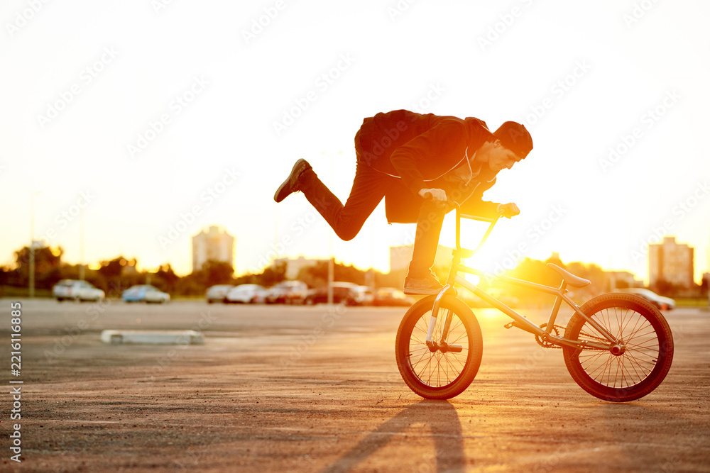 Naklejka premium City, sunset and trick with man on bicycle for adrenaline, exercise or extreme sports outdoor. Bike, flare and training with BMX rider on street in urban town for action, balance or hobby practice