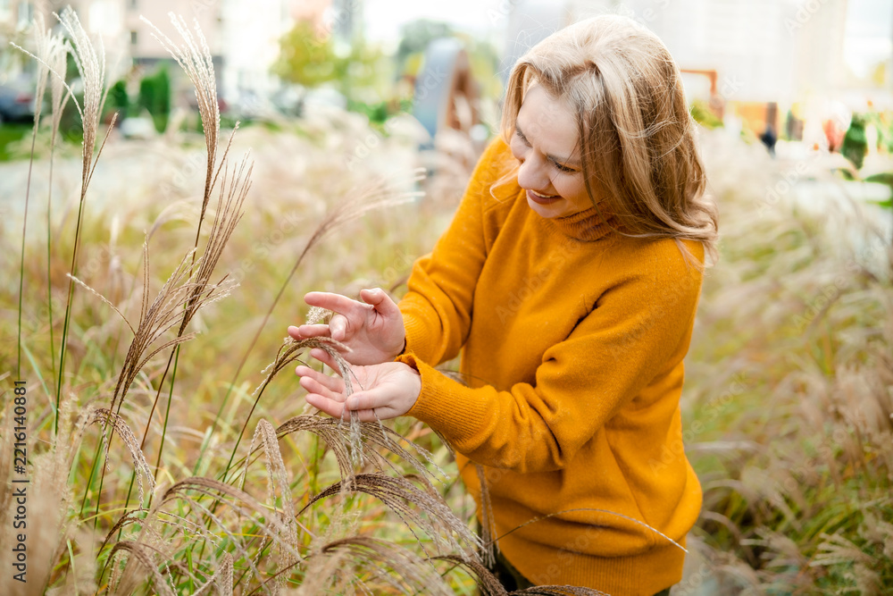 Fototapeta premium Cheerful woman in autumn nature with tall grass — mental wellbeing and ecotherapy concept. Joyful person enjoying fall season outdoor walk. Mindful connection with natural environment.