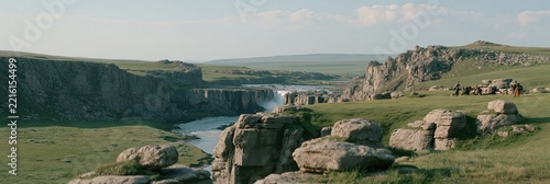 Waterfall cascading into a river in a rocky canyon with grassy hills