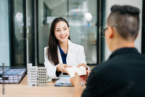 Asian female agent handing property agreement documents to a client in a modern office