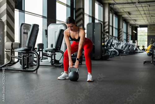 Fit brunette female athlete in red leggings exercising with kettlebell