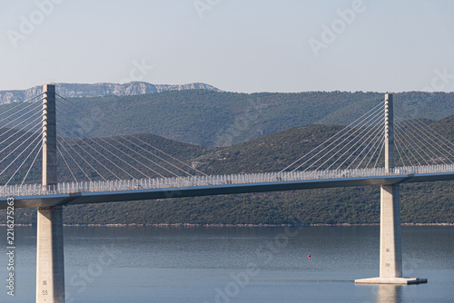 Symmetrical pylon of Peljesac Bridge reflected in calm bay, Croatia, clear day