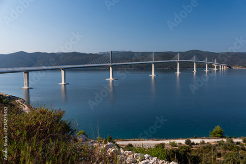 Panoramic view of Peljesac Bridge spanning deep blue bay from hillside, Croatia