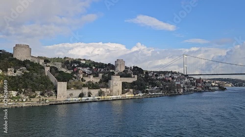 Ancient stone fortress lines the water edge. Modern bridge stretches across the wide river. Clouds drift above the historic cityscape in Istanbul, Turkey