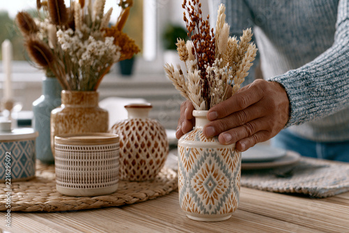 Close-up of young adult arranging dried flowers into handcrafted ceramic vases on a modern dining table, warm afternoon sunlight, , , , premium advertising quality