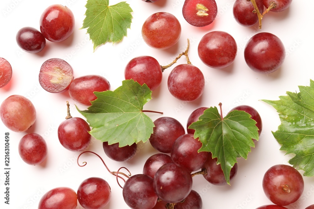 Fototapeta premium Fresh ripe grapes and green leaves on white background, flat lay