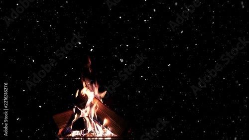 A campfire flickers as snow falls through the dark Christmas night, with space for text.