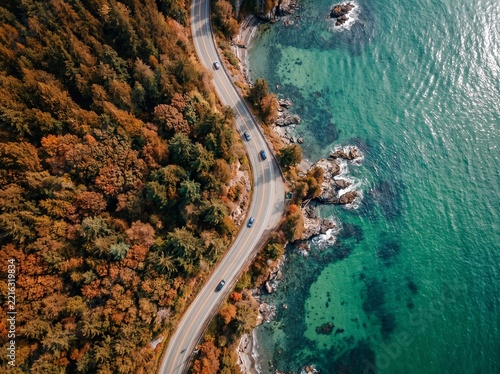 Aerial view of a winding coastal road beside a colorful autumn forest and turquoise sea with turquoise landscape vacation wilderness.