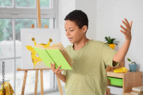 Education and literacy, young boy reading a book aloud with expressive gestur...