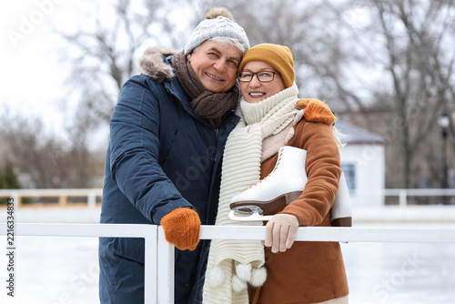 Senior couple with ice skates hugging at rink on winter day