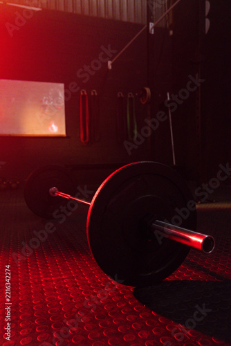 Loaded barbell resting on rubber coin flooring in gym, catching red accent light