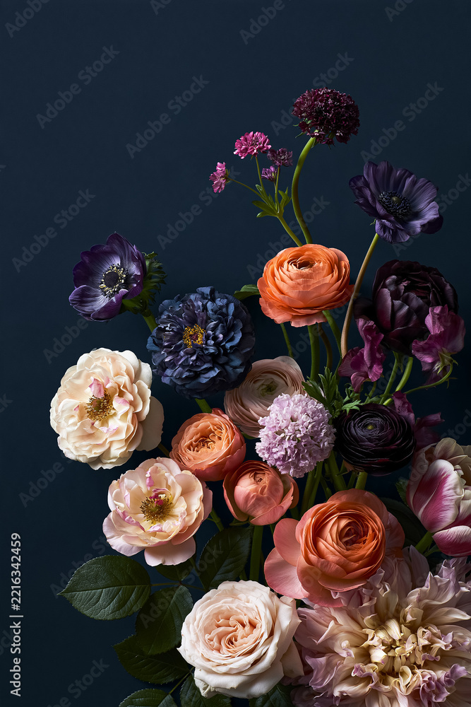 Naklejka premium Beautiful still life featuring a vibrant bouquet of various colorful flowers, including ranunculus, roses, and anemones, on a dark blue background