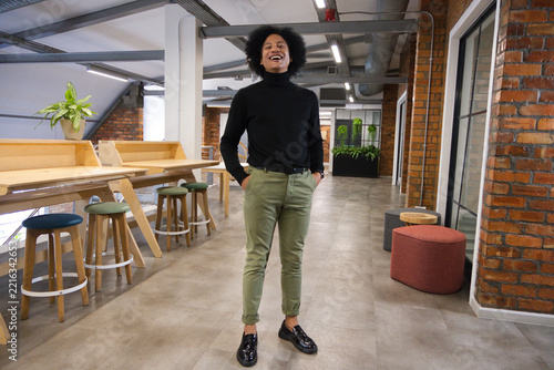 Man standing and laughing in coworking corridor by wooden workbench with plants