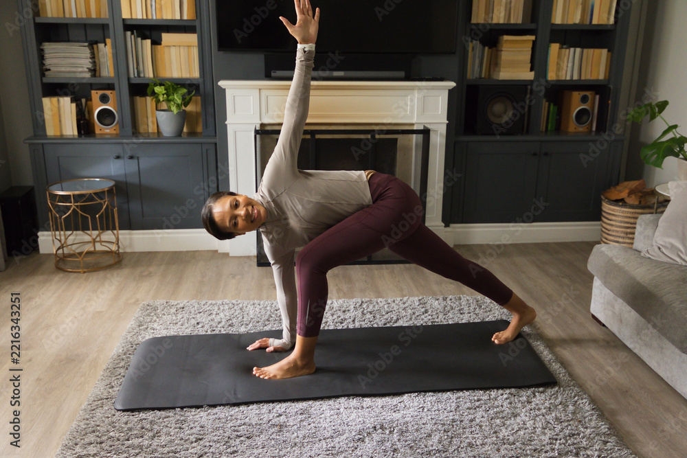 Fototapeta premium African American woman practicing side-angle in living room on mat in maroon leggings