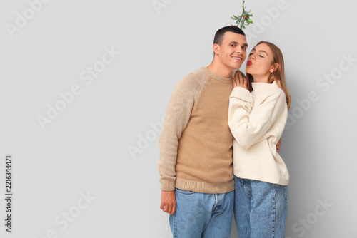Young couple hugging under mistletoe branch on light background