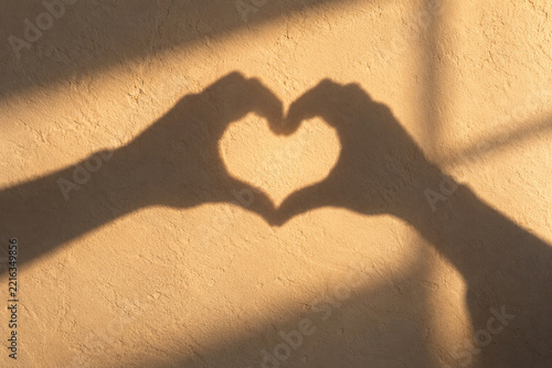 Heart shaped hand shadow on a warm sunlit textured wall