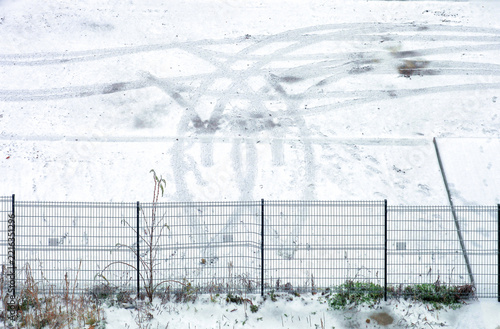 First winter snow covering parking lot ground with tire tracks and footprints