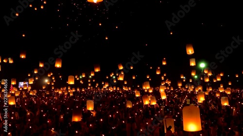 People gather at night to watch glowing lanterns float into the sky during a lantern release festival,