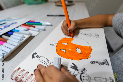 Child hand coloring halloween pumpkin drawing with orange marker