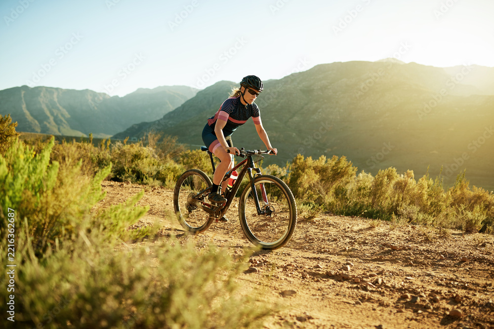 Fototapeta premium Woman, cycling and fitness with mountain bike for workout, cardio exercise or extreme outdoor sport. Active, female person or cyclist riding with bicycle on dirt road for training or health in nature