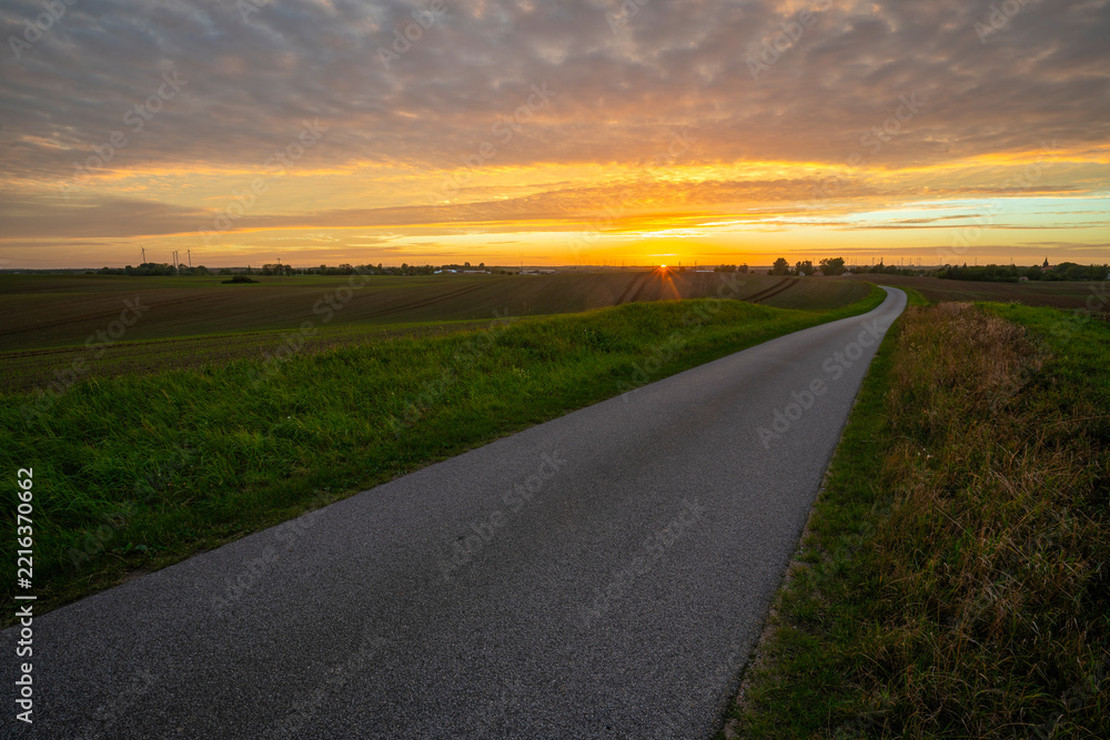 Fototapeta premium A rural, asphalt road in Germany at sunset