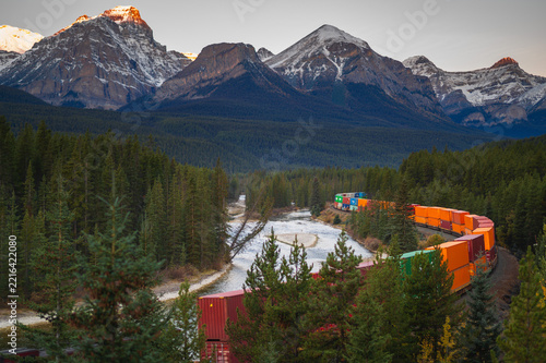 Majestic freight train carrying cargo travels through peaceful mountain forest and river in canada offering serene wilderness journey