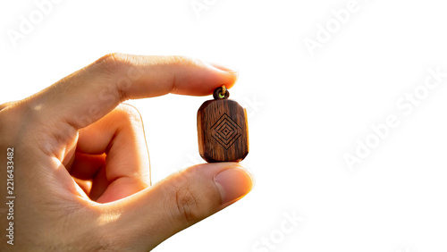 Hand holding a small rectangular wooden pendant with geometric engraving isolated on transparent background