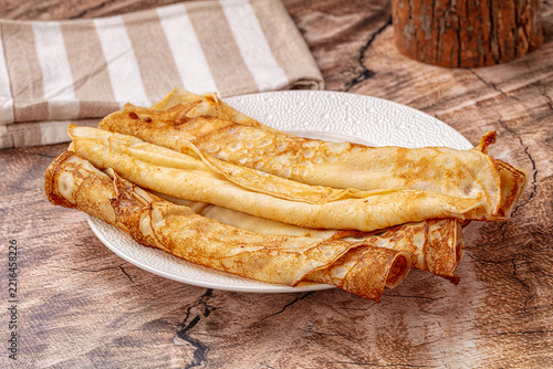 Breakfast dish golden brown pancakes folded on white textured plate, homemade thin crepes dessert