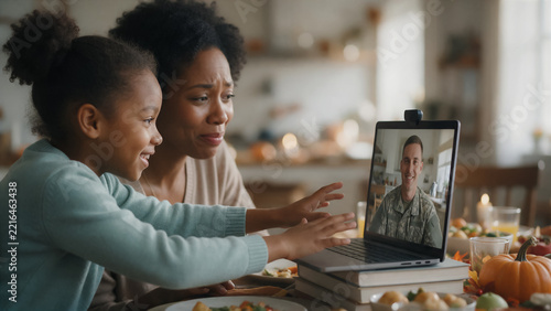 Staying in touch with loved ones far away, a laptop sits on a table set for Thanksgiving as a wife and her young daughter make a video call to her husband, copy space for text