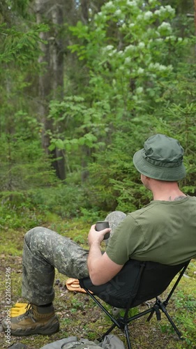 Man resting in a camping chair and drinking tea in a forest