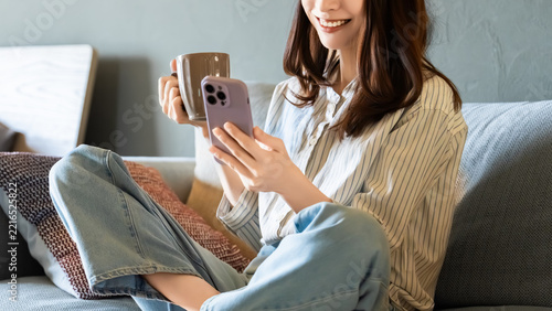 リビングのソファに座ってスマートフォンを使う女性