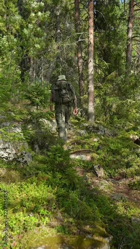 Hiker with backpack walking up a rocky trail in a sunny pine forest