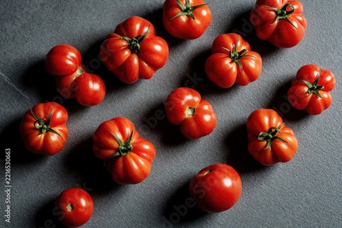 Group of irregular misshapen red tomatoes on dark grey stone table. Unusual deformed organic vegetables show imperfect produce concept. Healthy farm food with weird shapes ready for cooking. Ugly