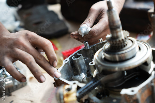 Selective focus on mechanic hands applying liquid gasket silicone sealant tube onto a motorcycle engine crankcase before assembly.