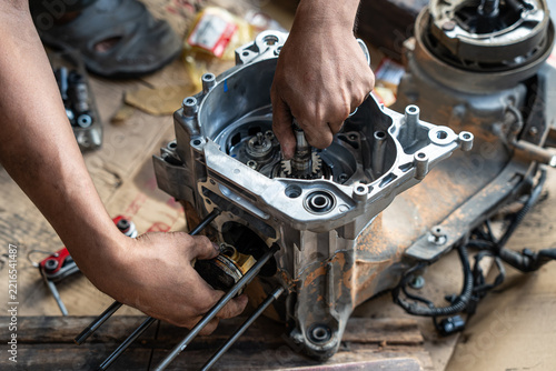 High angle close-up view of a skilled auto mechanic using hands to carefully align and install a crankshaft and piston assembly inside an aluminum motorcycle crankcase during an engine overhaul.