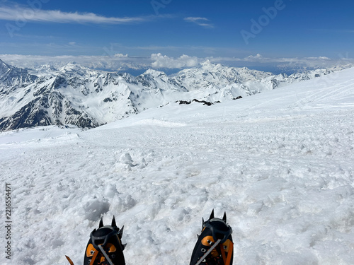 Climber's feet in high-altitude boots and crampons on a snowy slope, first-person view
