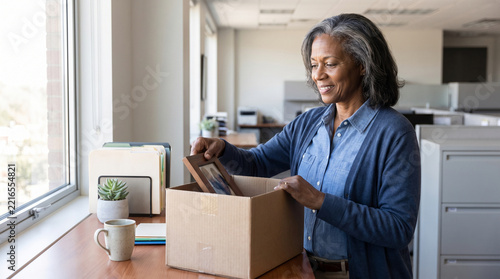 A Black woman gathers her belongings from her desk on her last day at the office before retiring.