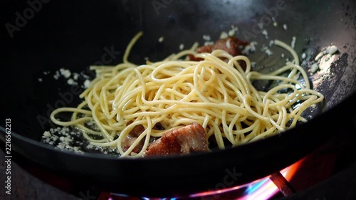 4K Chef using a red silicone spatula to stir fry spaghetti pasta with bacon in a hot wok over stove flame, cooking process for Italian spaghetti carbonara dish.