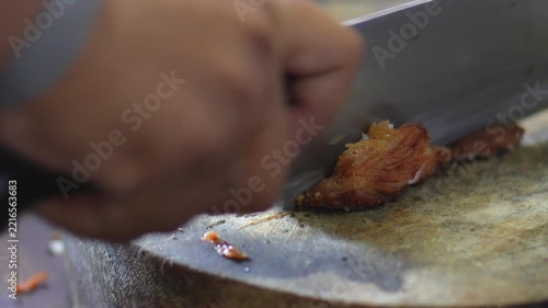 4K Chef hand using a sharp cleaver knife to chop crispy roasted pork on a wooden cutting board, showing food preparation process for Asian cuisine.