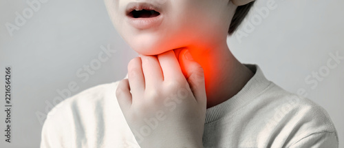 A child stands at home, touching their throat with a worried loo