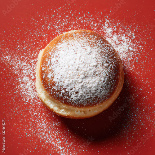 Deliciously Soft and Fluffy Donut Dusting with Powdered Sugar on Vibrant Red Background