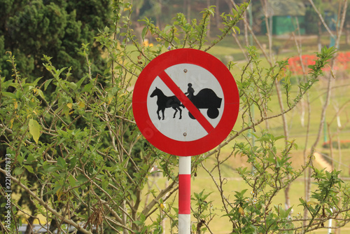 Obraz na plátně Close up of a round red and white no horse-drawn carriages allowed traffic sign surrounded by green bushes in Da Lat, Vietnam