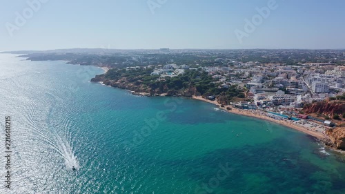 Stunning aerial perspective of a speedboat sailing on the turquoise atlantic ocean along the beautiful coastline of olhos de agua in algarve, portugal, on a bright sunny day