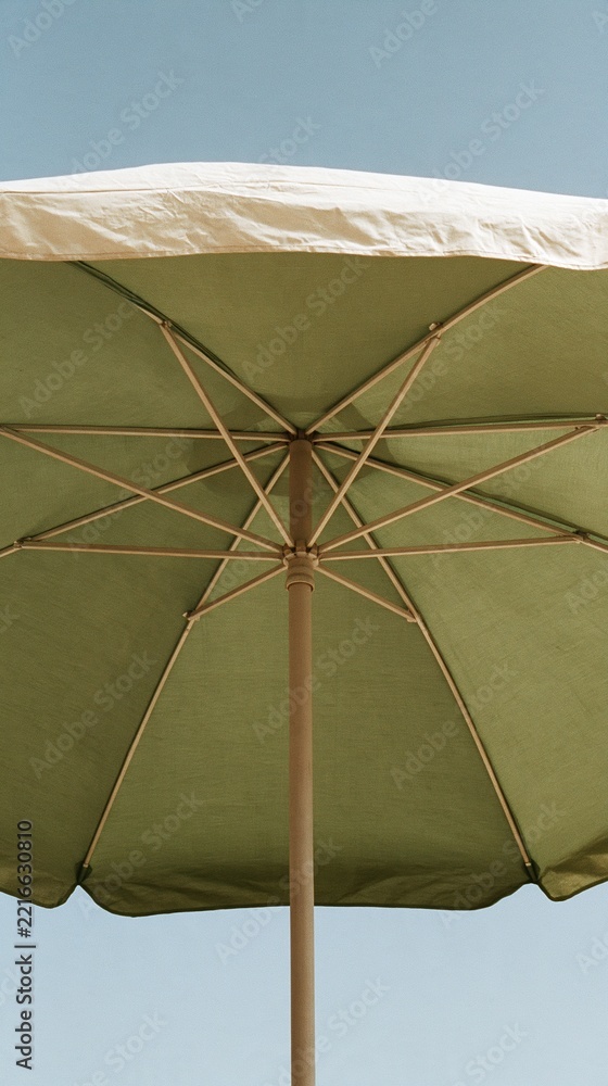 Fototapeta premium Close-up view from below of a light green outdoor patio umbrella with wooden pole against a clear blue sky